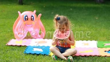 小女孩吃西瓜。 婴儿在夏天吃食物。 在绿草或草坪上野餐